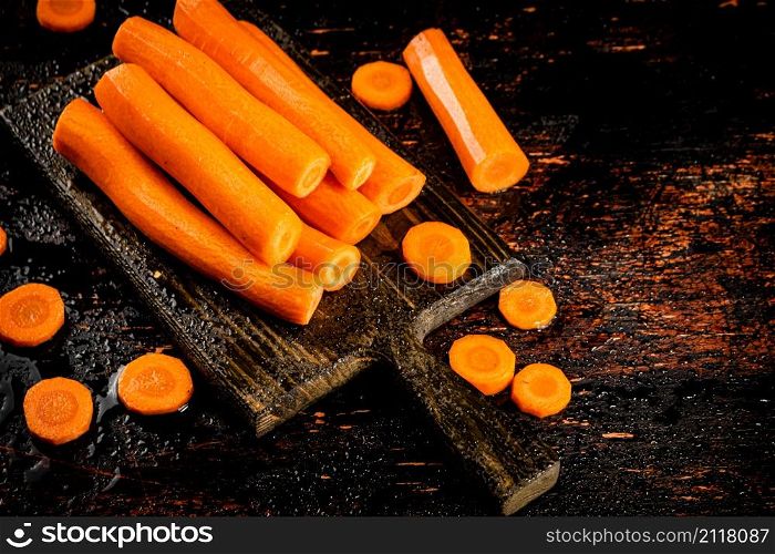 Pieces and whole fresh carrots on a cutting board. Against a dark background. High quality photo. Pieces and whole fresh carrots on a cutting board.