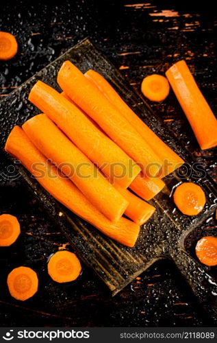 Pieces and whole fresh carrots on a cutting board. Against a dark background. High quality photo. Pieces and whole fresh carrots on a cutting board.