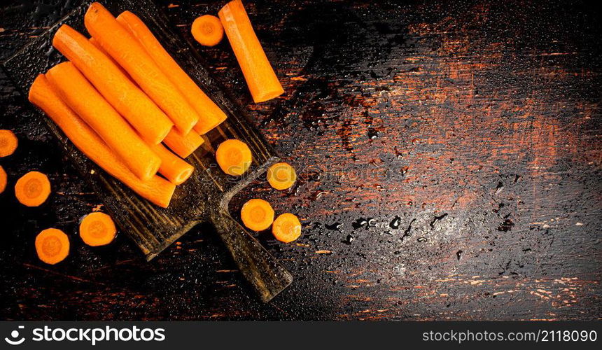 Pieces and whole fresh carrots on a cutting board. Against a dark background. High quality photo. Pieces and whole fresh carrots on a cutting board.