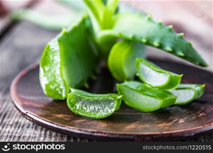 Pieces of aloe vera and fresh leaves lie on a bowl against the background of old boards. Treatment and skin care.. Pieces of aloe vera and fresh leaves lie on a bowl against the background of old boards.