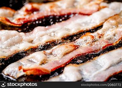 Pieces of bacon are fried in boiling oil with air bubbles. On a black background. High quality photo. Pieces of bacon are fried in boiling oil with air bubbles.