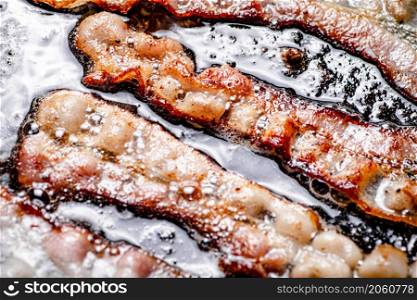 Pieces of bacon are fried in boiling oil with air bubbles. On a black background. High quality photo. Pieces of bacon are fried in boiling oil with air bubbles.