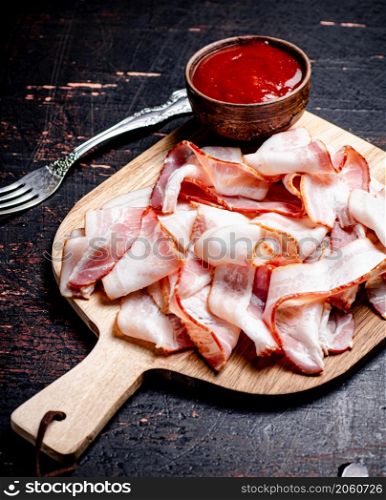 Pieces of bacon on a cutting board with tomato sauce. Against a dark background. High quality photo. Pieces of bacon on a cutting board with tomato sauce.