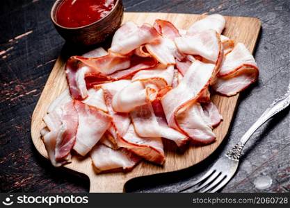 Pieces of bacon on a cutting board with tomato sauce. Against a dark background. High quality photo. Pieces of bacon on a cutting board with tomato sauce.