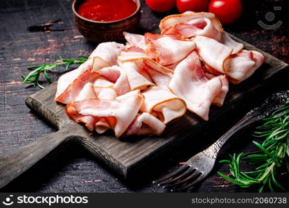 Pieces of bacon on a cutting board with tomato sauce. Against a dark background. High quality photo. Pieces of bacon on a cutting board with tomato sauce.