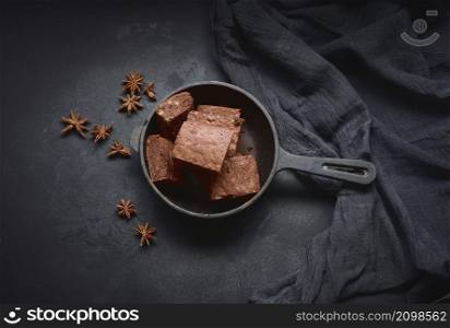 pieces of baked brownie in a metal black frying pan on the table, top view