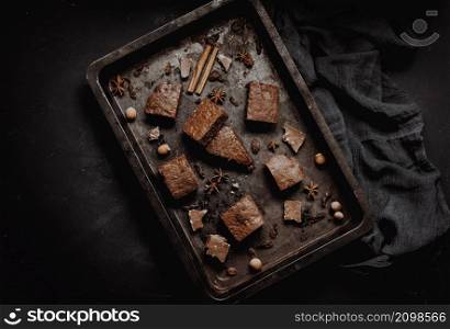pieces of baked chocolate brownie pie in a metal baking sheet on a black table, top view