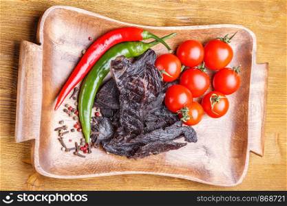 Pieces of beef jerky, tomatoes, hot pepper and spices on a wooden tray. Pieces of beef jerky, tomatoes, hot pepper and spices on a wooden tray on a wooden table