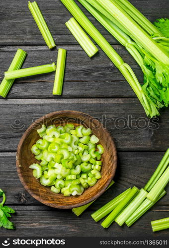 Pieces of celery in a wooden bowl. On black wooden background. Pieces of celery in a wooden bowl.