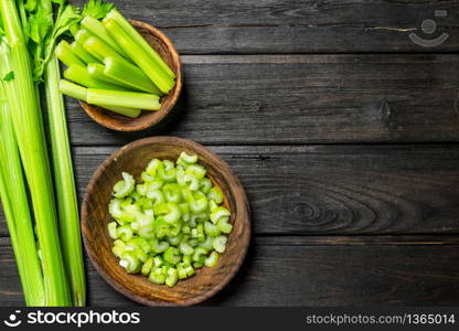 Pieces of celery in a wooden bowl. On black wooden background. Pieces of celery in a wooden bowl.