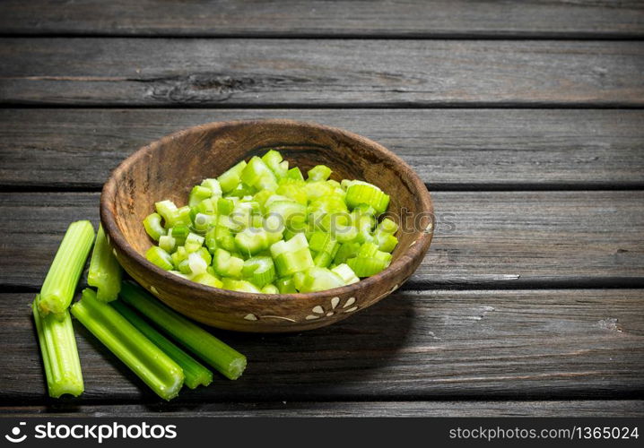 Pieces of celery in a wooden bowl. On black wooden background. Pieces of celery in a wooden bowl.