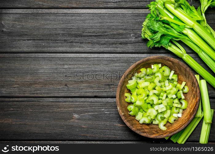 Pieces of celery in a wooden bowl. On black wooden background. Pieces of celery in a wooden bowl.