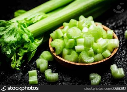 Pieces of celery in a wooden plate on the table. On a black background. High quality photo. Pieces of celery in a wooden plate on the table.
