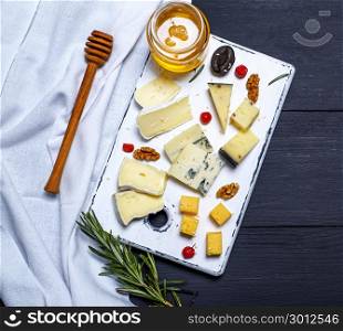 pieces of cheese on a white board and a glass jar with honey, top view