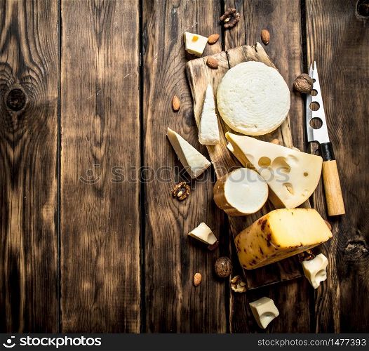 Pieces of cheese with nuts on a Board with a knife. On a wooden table.. Pieces of cheese with nuts
