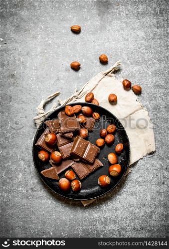 Pieces of chocolate with nuts on the old plate. On the black wooden table.. Pieces of chocolate with nuts on the old plate.