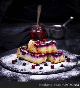 pieces of cottage cheese pie with blueberry berries are sprinkled with sugar powder, behind the jar with jam, black background
