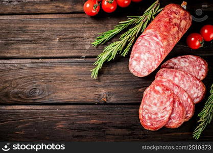 Pieces of delicious salami sausage with rosemary and tomatoes. On a wooden background. High quality photo. Pieces of delicious salami sausage with rosemary and tomatoes.