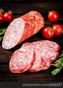 Pieces of delicious salami sausage with rosemary and tomatoes. On a wooden background. High quality photo. Pieces of delicious salami sausage with rosemary and tomatoes.
