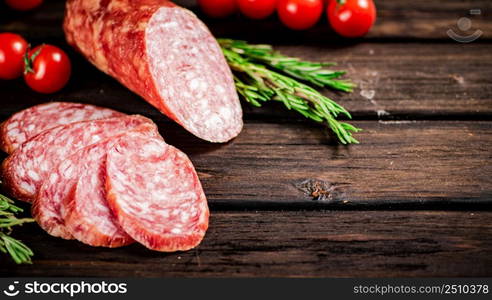 Pieces of delicious salami sausage with rosemary and tomatoes. On a wooden background. High quality photo. Pieces of delicious salami sausage with rosemary and tomatoes.