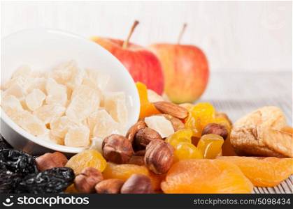 Pieces of dried pineapple, apricot, nuts and red apples on a wooden background. Various fruit snacks.