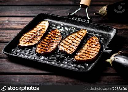 Pieces of eggplant grilled in a grill pan. On a wooden background. High quality photo. Pieces of eggplant grilled in a grill pan.