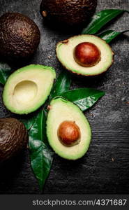 Pieces of fresh avocado with leaves on a stone board. On a black background. High quality photo. Pieces of fresh avocado with leaves on a stone board.