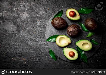 Pieces of fresh avocado with leaves on a stone board. On a black background. High quality photo. Pieces of fresh avocado with leaves on a stone board.