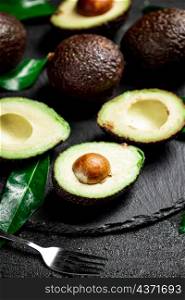 Pieces of fresh avocado with leaves on a stone board. On a black background. High quality photo. Pieces of fresh avocado with leaves on a stone board.