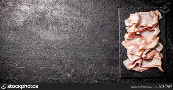 Pieces of fresh bacon on a stone board. On a black background. High quality photo. Pieces of fresh bacon on a stone board.