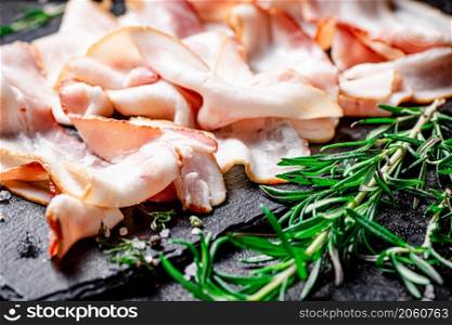 Pieces of fresh bacon with rosemary. On a black background. High quality photo. Pieces of fresh bacon with rosemary.