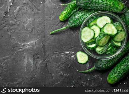 Pieces of fresh cucumbers in a glass bowl. On black rustic background. Pieces of fresh cucumbers in a glass bowl.