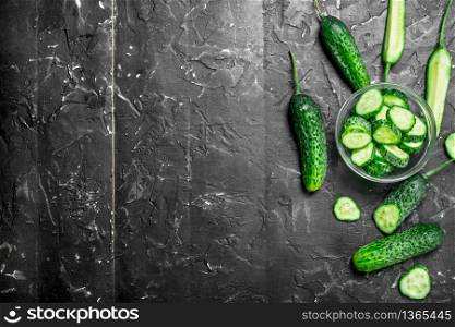Pieces of fresh cucumbers in a glass bowl. On black rustic background. Pieces of fresh cucumbers in a glass bowl.