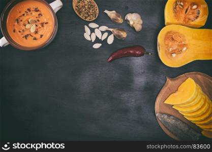 pieces of fresh pumpkin and pumpkin soup on a black background, empty space in the middle