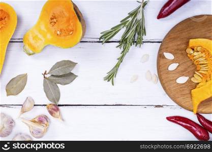pieces of fresh pumpkin and spices on a white wooden background, empty space in the middle