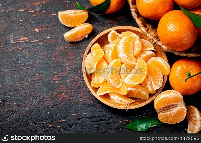 Pieces of fresh tangerines on a plate with leaves. On a rustic dark background. High quality photo. Pieces of fresh tangerines on a plate with leaves.