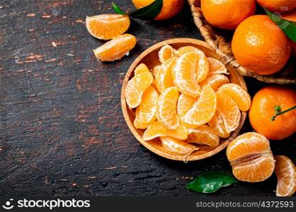 Pieces of fresh tangerines on a plate with leaves. On a rustic dark background. High quality photo. Pieces of fresh tangerines on a plate with leaves.