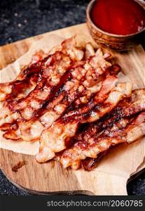 Pieces of fried bacon on a wooden cutting board. On a black background. High quality photo. Pieces of fried bacon on a wooden cutting board.