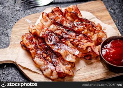 Pieces of fried bacon on a wooden cutting board. On a black background. High quality photo. Pieces of fried bacon on a wooden cutting board.