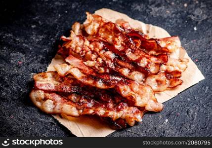 Pieces of fried bacon on paper. On a black background. High quality photo. Pieces of fried bacon on paper.