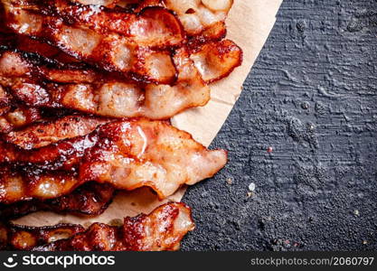 Pieces of fried bacon on paper. On a black background. High quality photo. Pieces of fried bacon on paper.