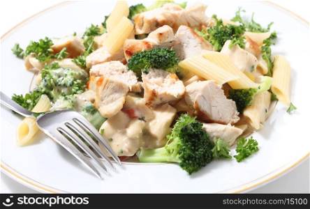 Pieces of grilled chicken served with penne pasta in a broccoli, capsicum and garlic cheese sauce, garnished with parsley.