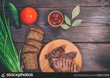 Pieces of grilled veal, brown wooden background, vintage toning
