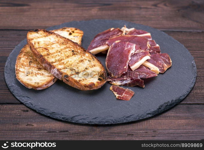 pieces of jamon and bread toast on a black background, top view