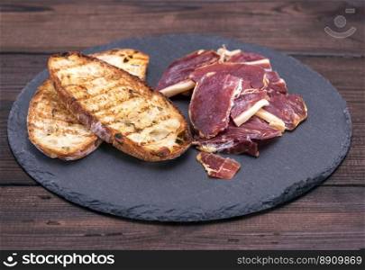 pieces of jamon and bread toast on a black background, top view