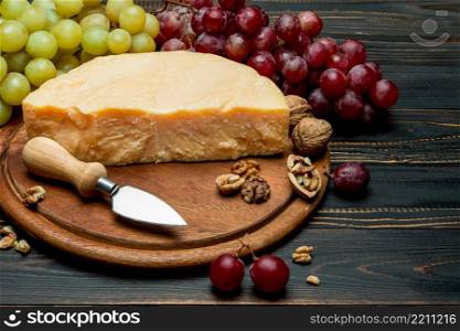 pieces of parmesan or parmigiano hard cheese and grapes on wooden cutting board. pieces of parmesan or parmigiano cheese and grapes