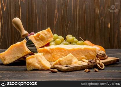 pieces of parmesan or parmigiano hard cheese and grapes on wooden cutting board. pieces of parmesan or parmigiano cheese and grapes