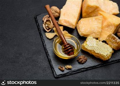 pieces of parmesan or parmigiano hard cheese and honey on dark concrete background. pieces of parmesan or parmigiano cheese and honey
