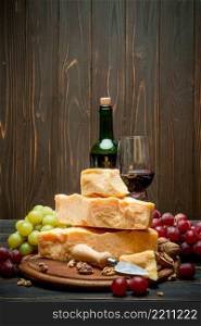 pieces of parmesan or parmigiano hard cheese, grapes and wine on wooden cutting board. pieces of parmesan or parmigiano cheese, grapes and wine