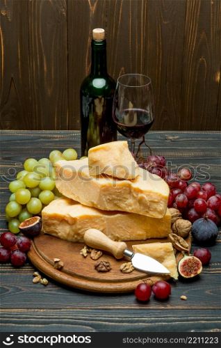 pieces of parmesan or parmigiano hard cheese, grapes and wine on wooden cutting board. pieces of parmesan or parmigiano cheese, grapes and wine